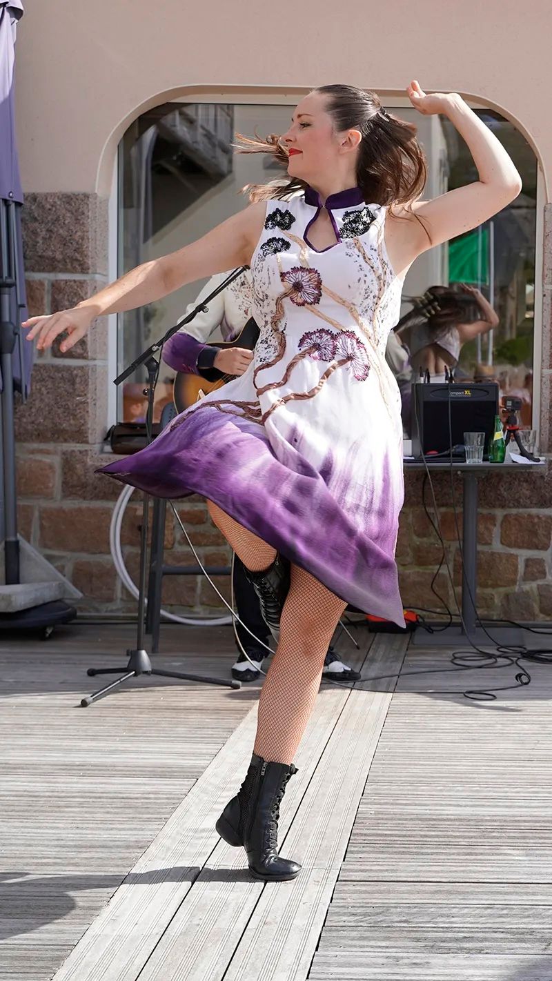 En plein jour, sur une terrasse, la danseuse tourne, les bras ouverts, la robe en mouvement.