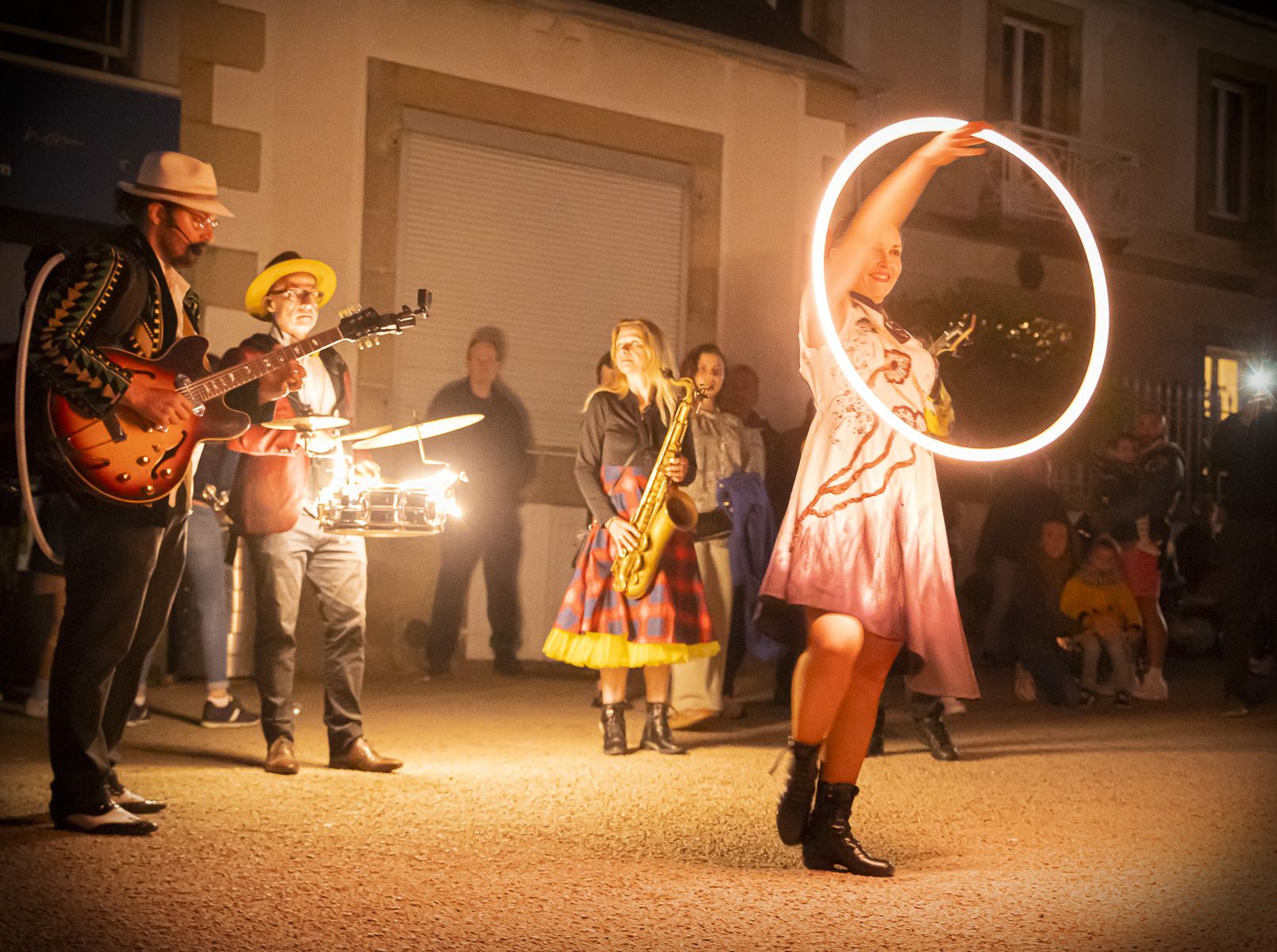 Un soir d’été, une danseuse de Streetside lève son hoop lumineux au milieu de la rue, devant les musiciens et le public.