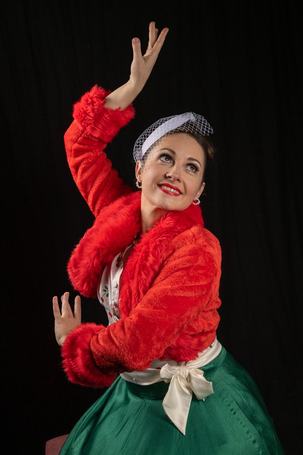 Fanny Viss, veste rouge et jupe verte, une main levée au-dessus de la tête.