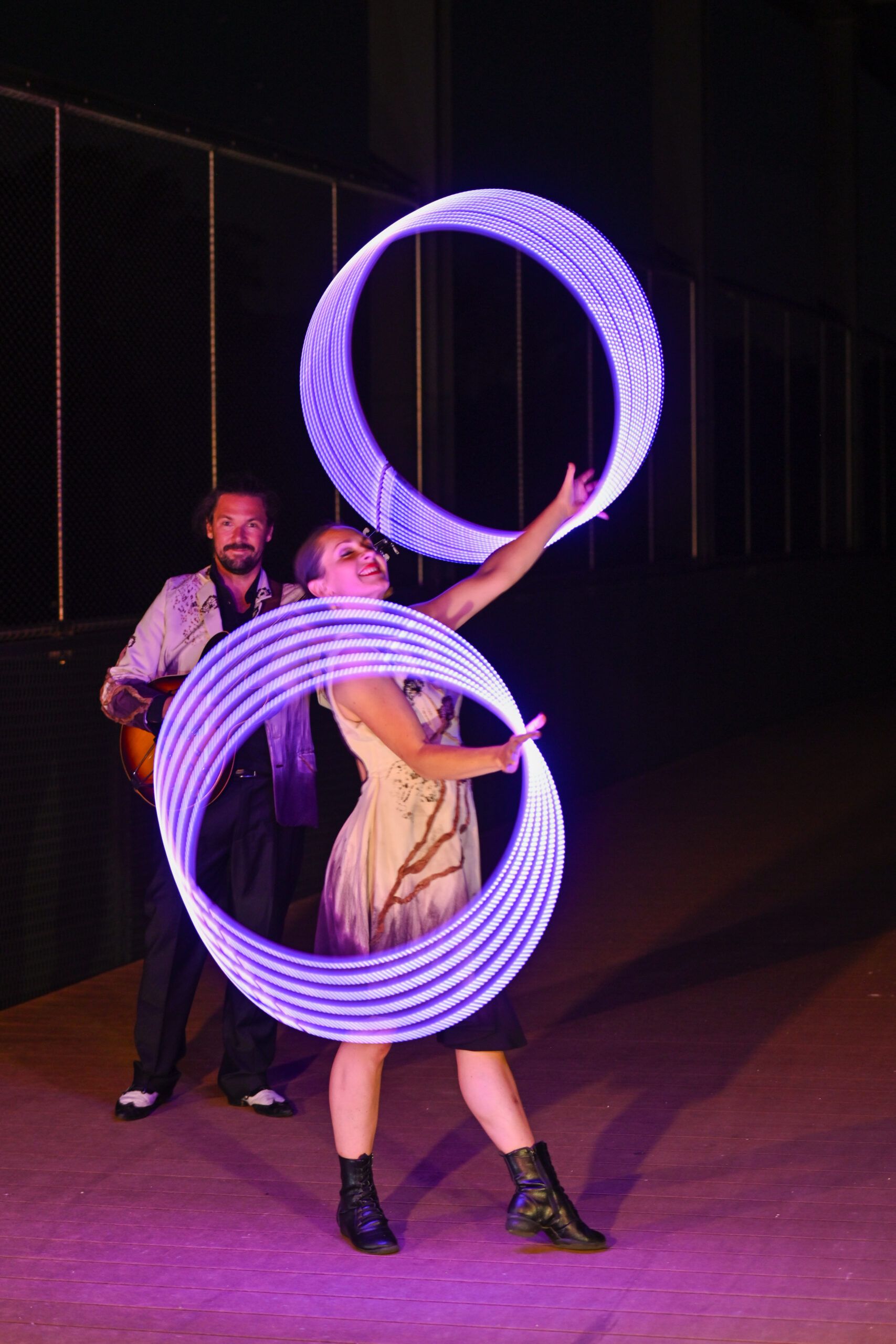 La nuit, la danseuse fait tourner deux cerceaux lumineux à côté du guitariste.