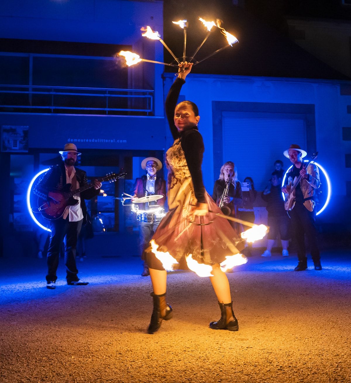 La nuit, une danseuse fait tourner un éventail de feu devant les musiciens et leurs hoops lumineux.