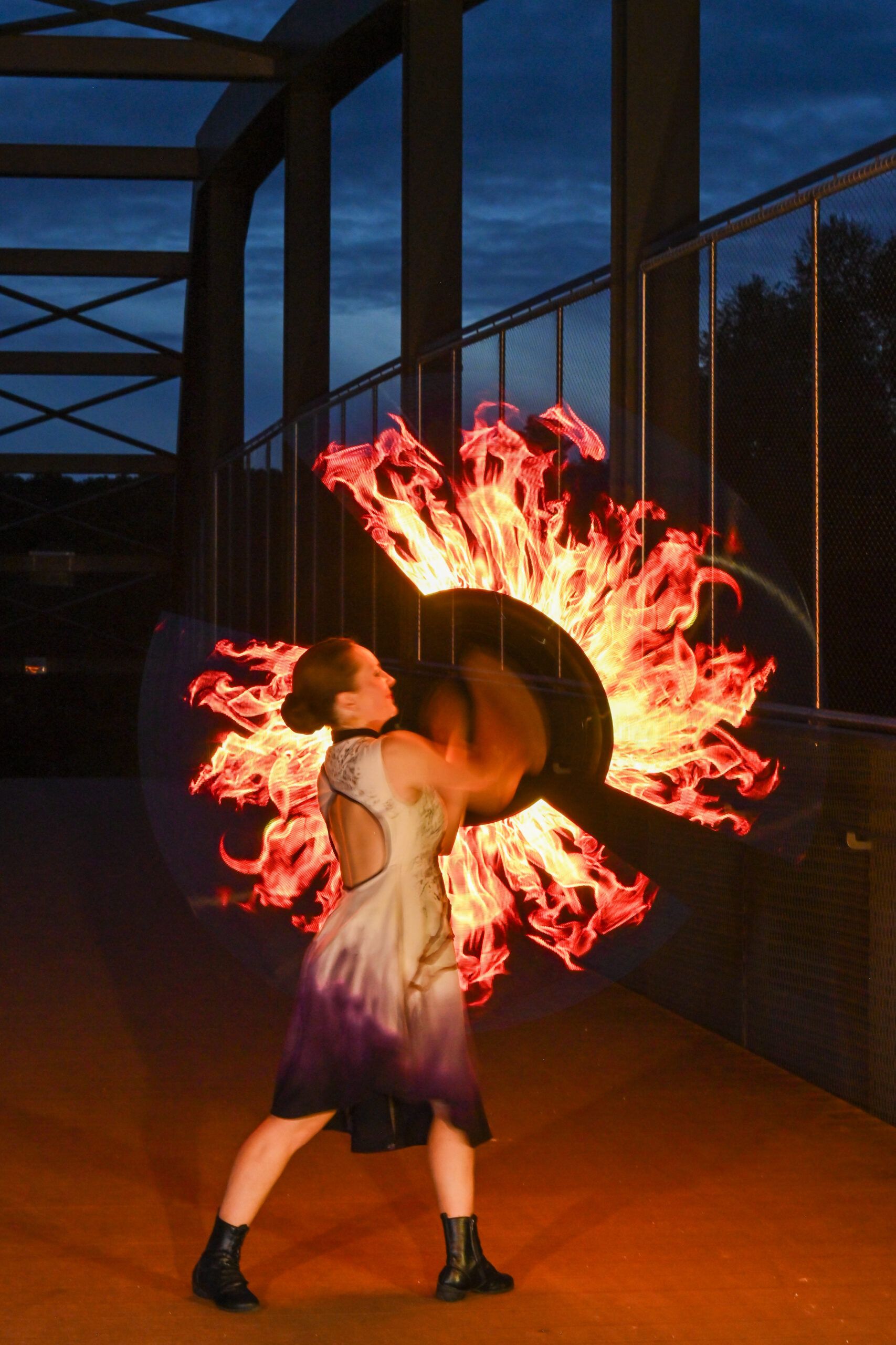 À la tombée de la nuit, la danseuse, de dos, ouvre deux éventails de feu qui dessinent une roue de flammes.