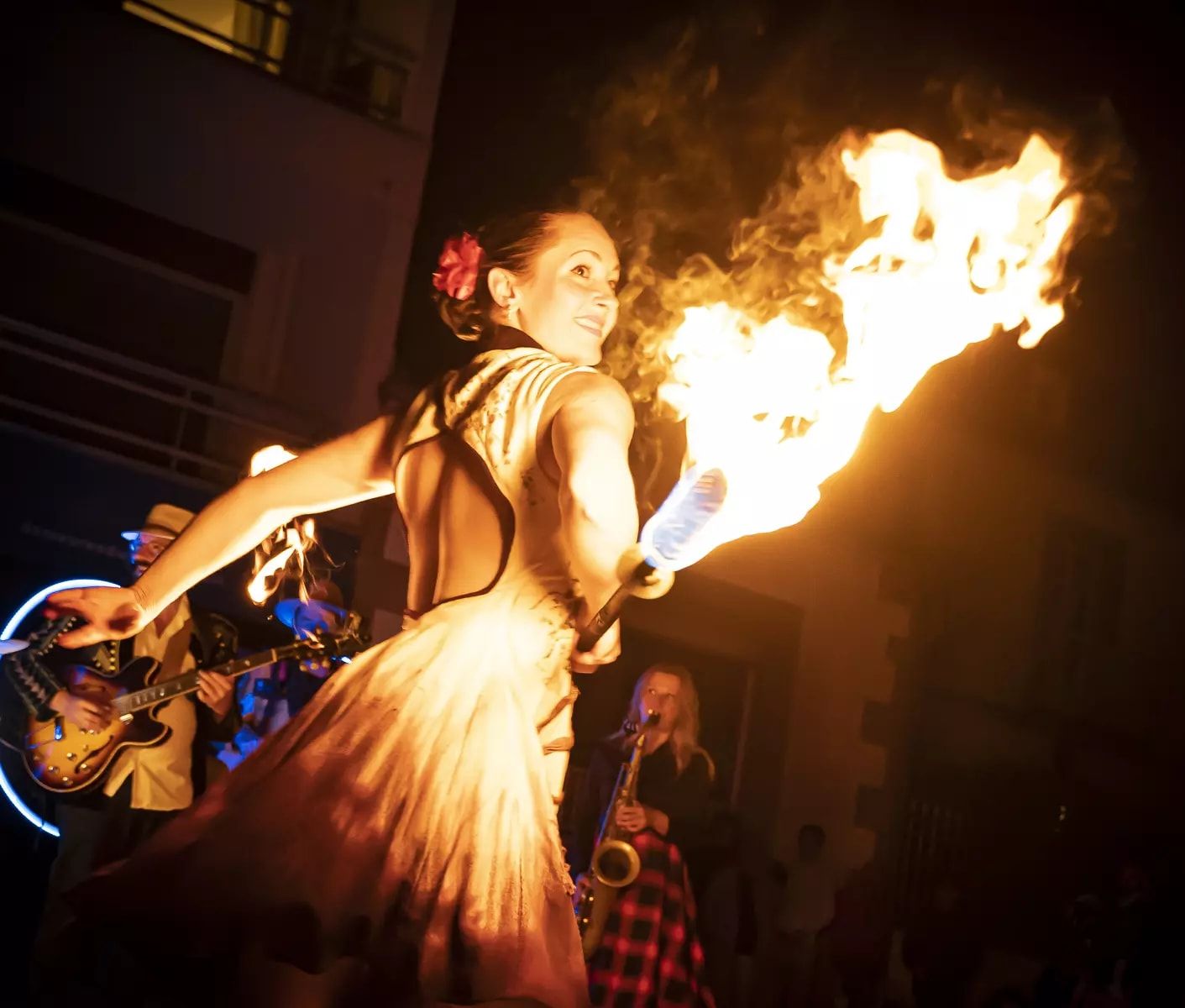 La nuit, la danseuse tourne en souriant, une fleur rouge dans les cheveux ; une grande flamme part de sa main.