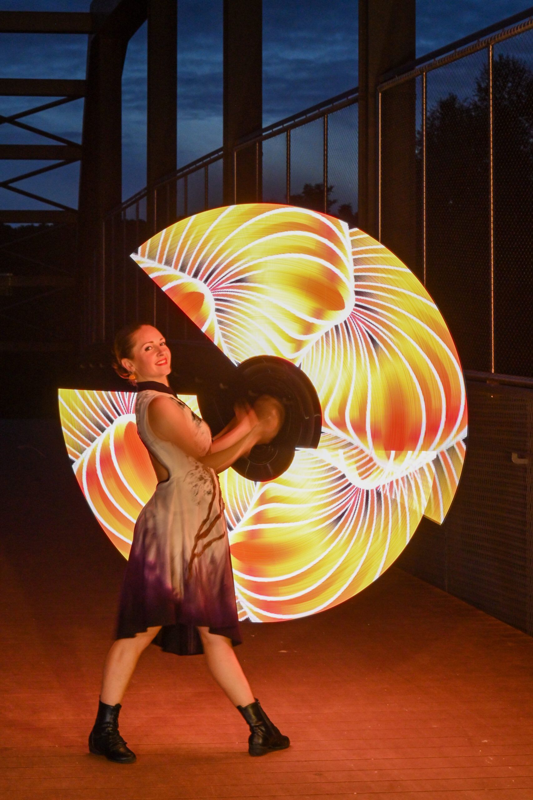 La danseuse fait tourner deux éventails lumineux, qui dessinent une grande roue de lumière dorée.