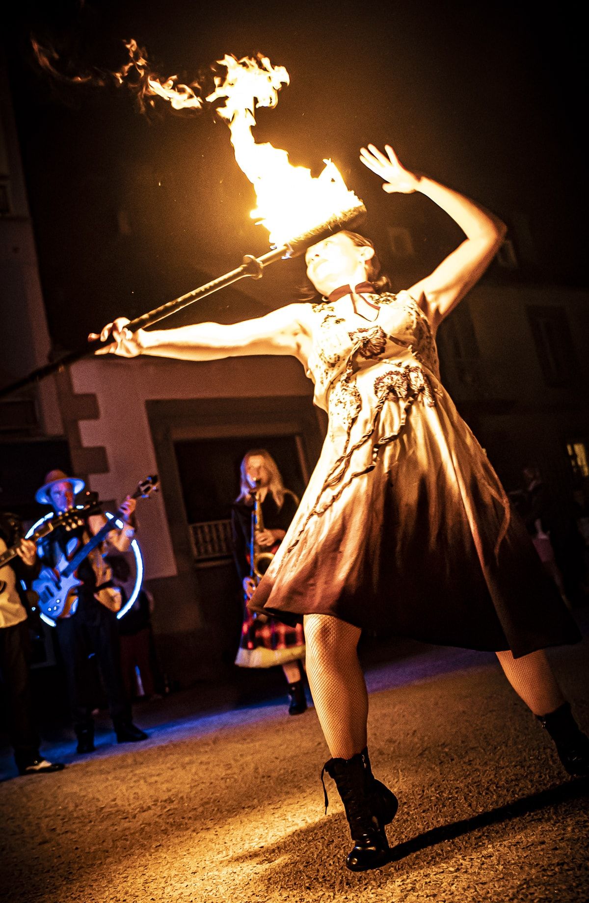 La nuit, une danseuse lève son bâton de feu au-dessus d’elle, les flammes au bout du bras, devant les musiciens.