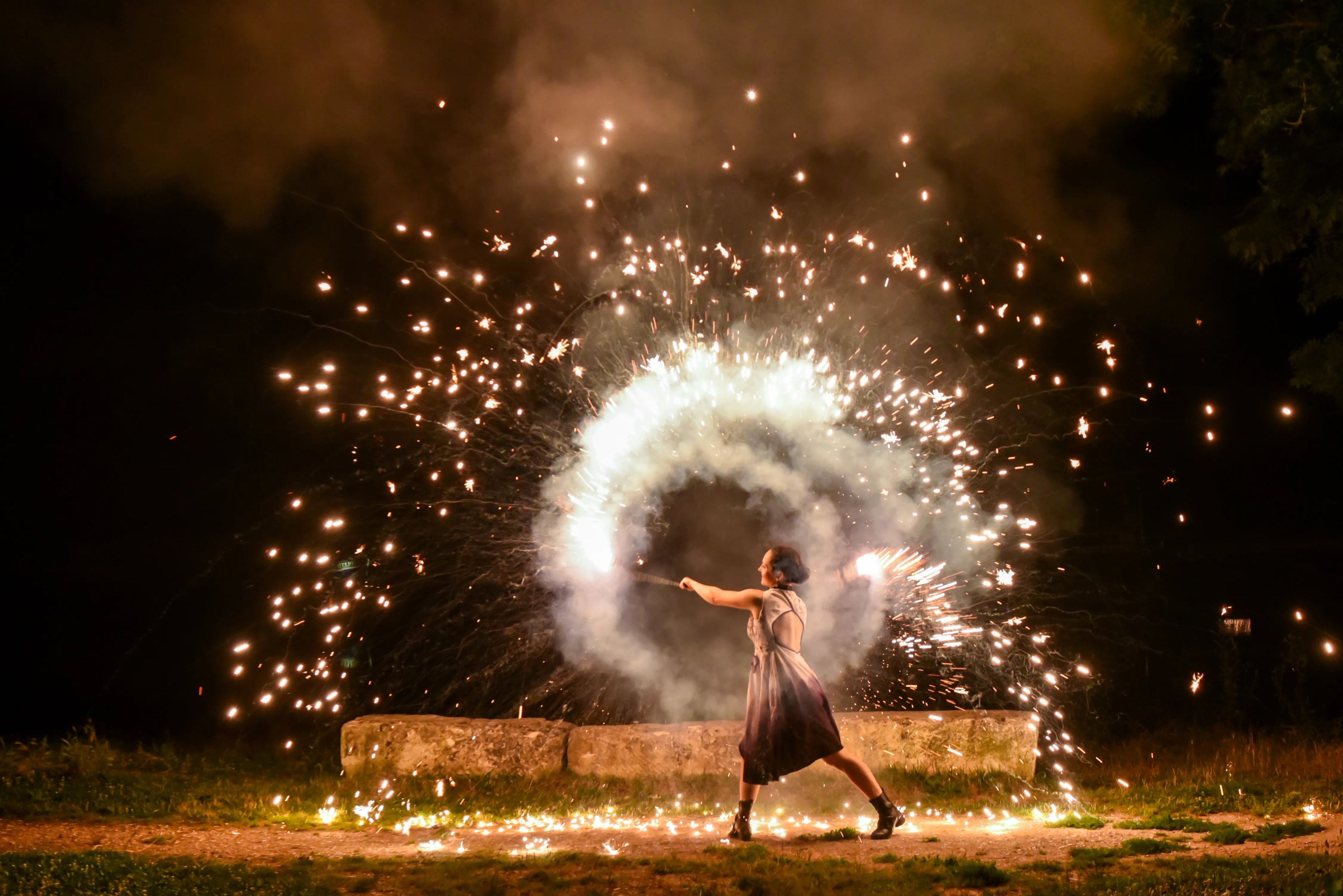 La nuit, la danseuse fait tourner un artifice : une gerbe d’étincelles et de fumée blanche s’ouvre en cercle autour d’elle.