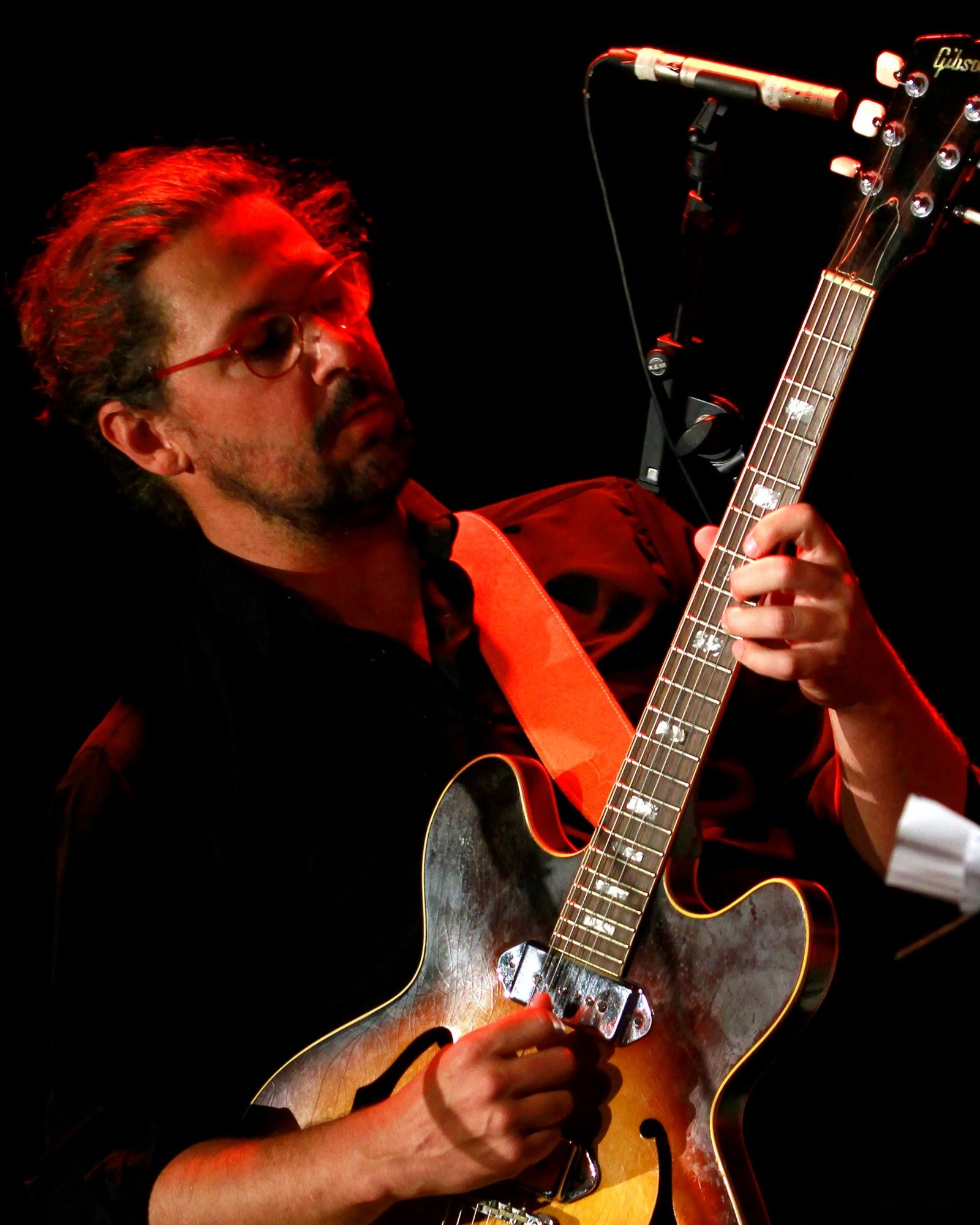 Le guitariste sur scène, dans une lumière rouge, penché sur sa guitare.
