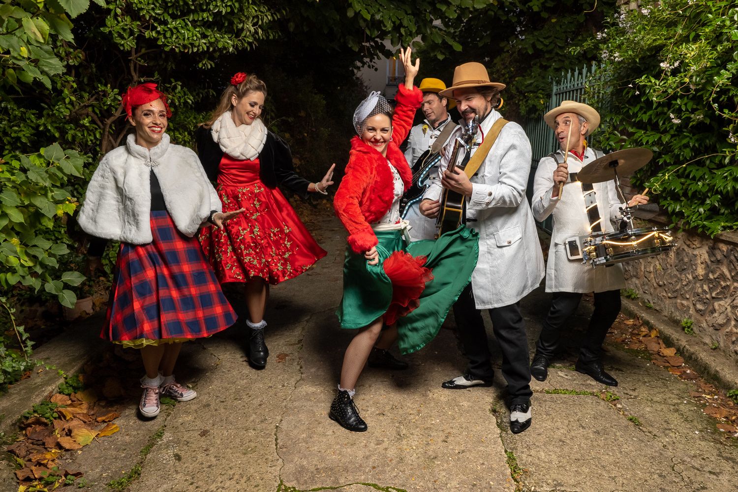 Les danseuses de Streetside en capes blanches et jupes écossaises, avec les musiciens, dans un jardin.