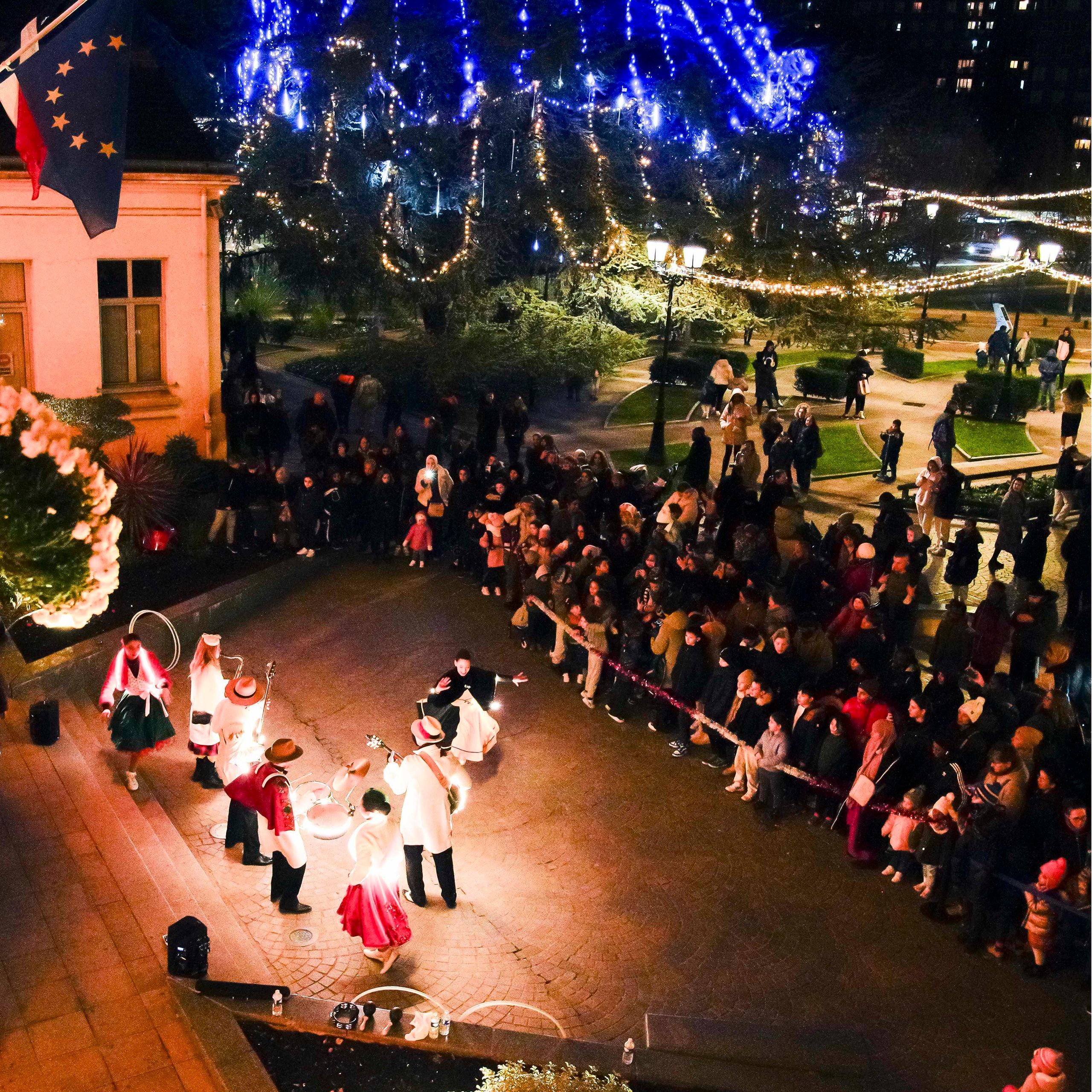 Vue d’en haut : Streetside joue sur une place illuminée pour Noël, entourée par le public.