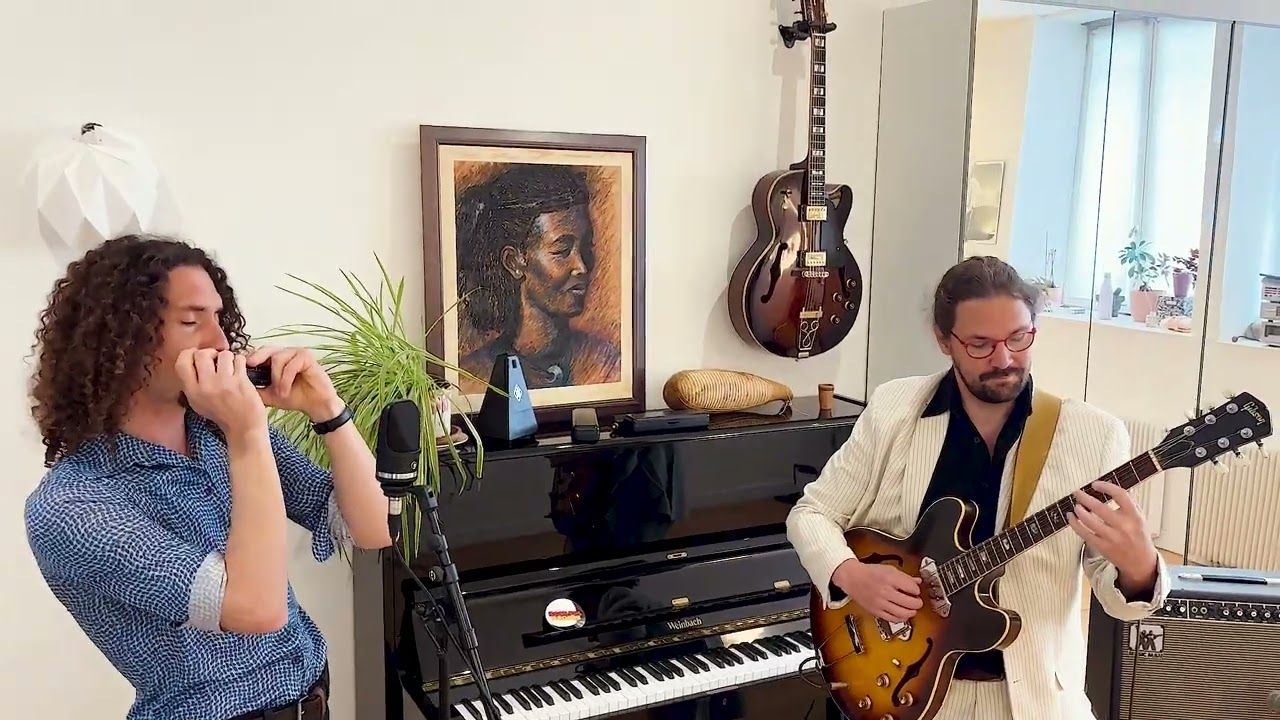 Le duo joue dans un salon, de part et d’autre d’un piano droit : Thomas Laurent à l’harmonica, de profil, Mathieu Crochemore à la guitare.