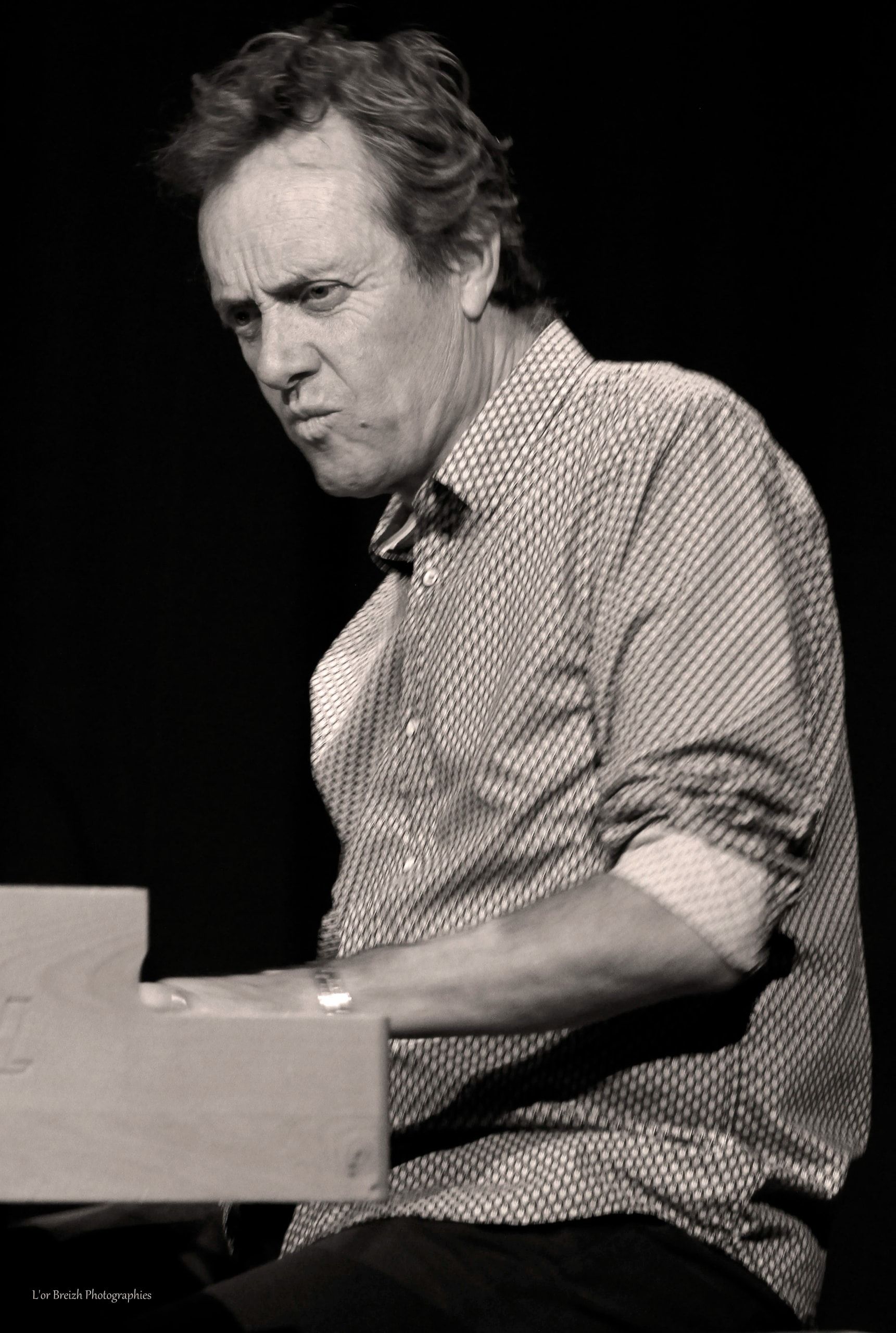 Sur scène, en noir et blanc, Jean-Pat Cosset joue de l’orgue, le visage concentré, les manches retroussées.