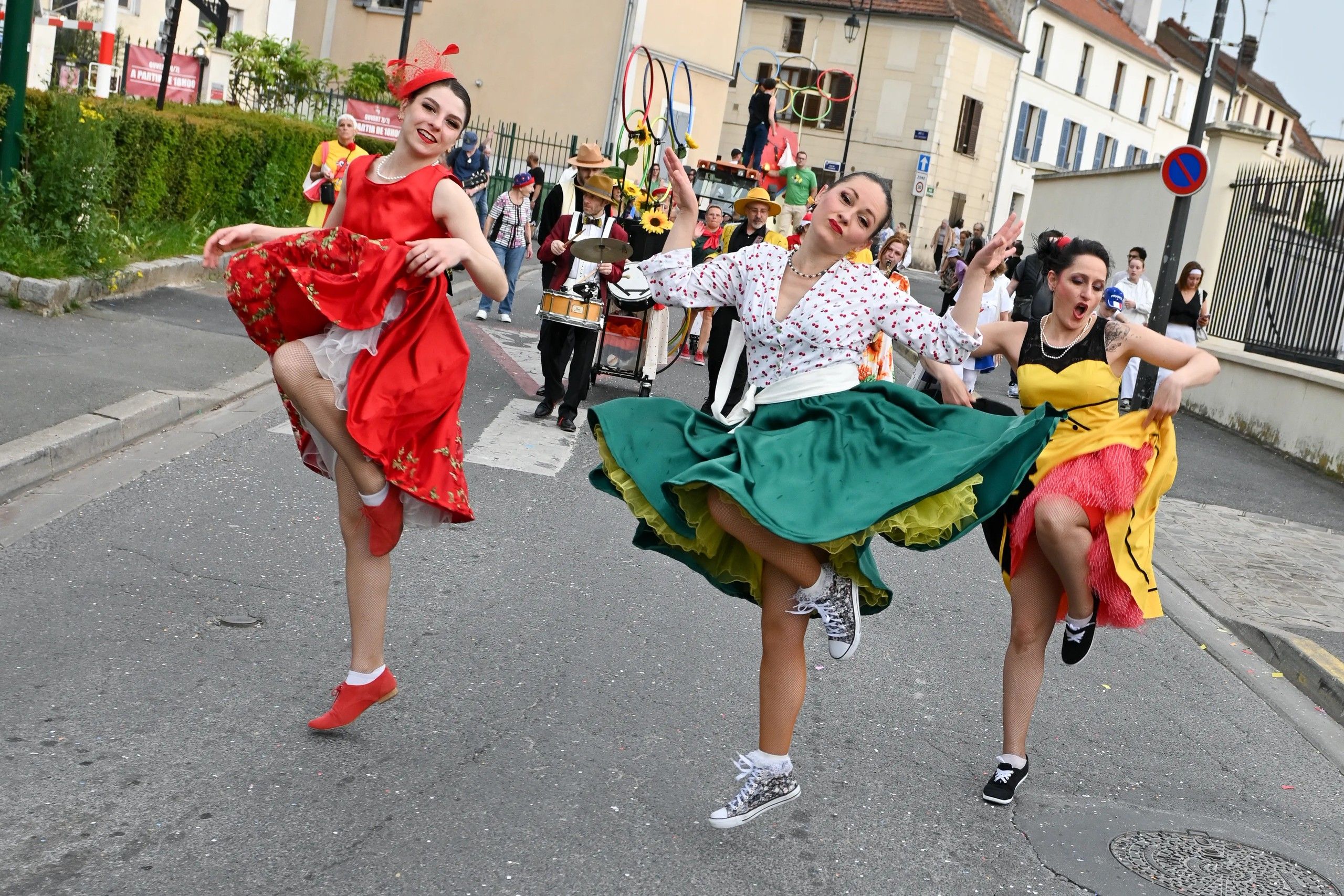 Trois danseuses de Streetside lèvent la jambe en rythme dans la rue, devant les musiciens du cortège.