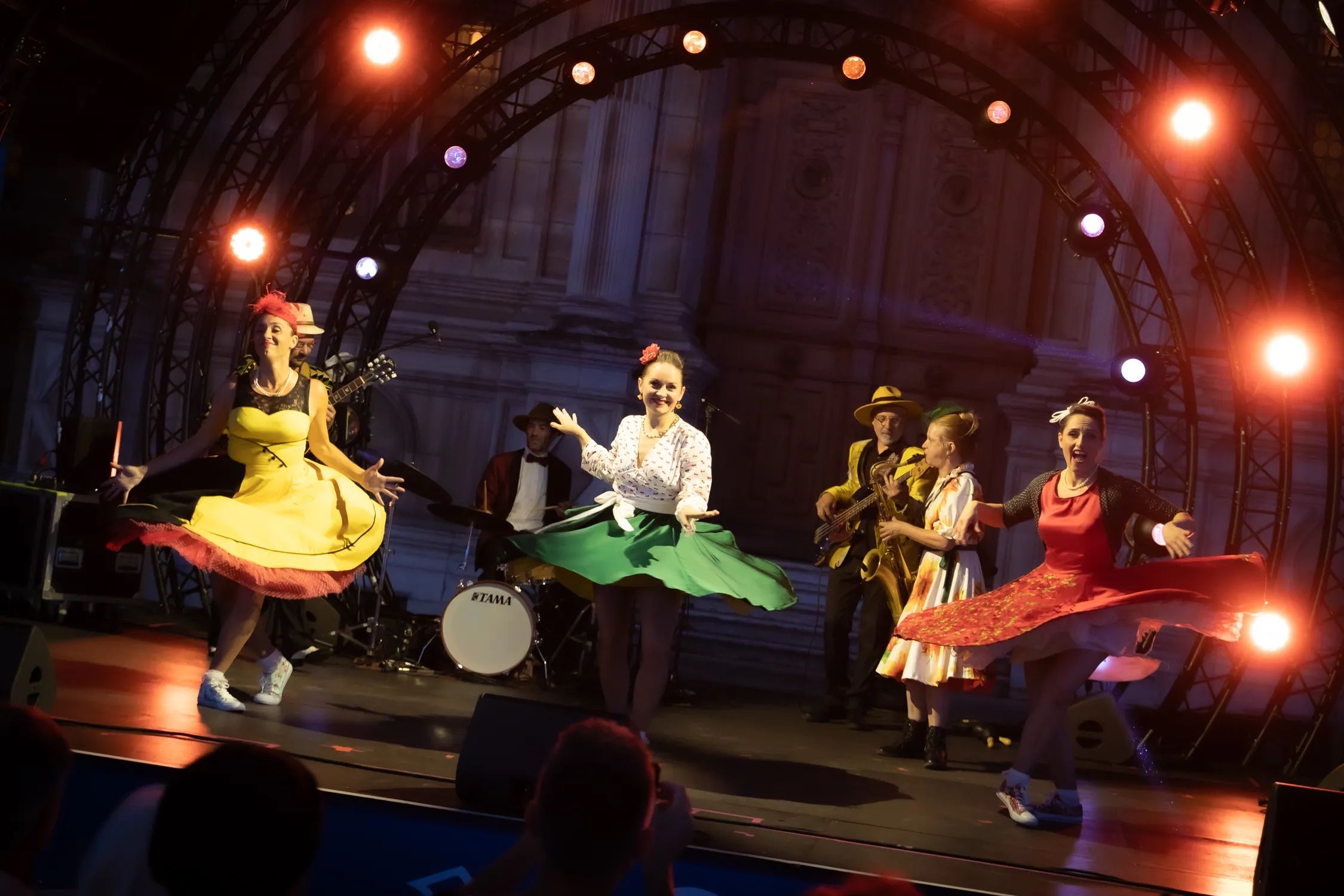 Sur une grande scène en plein air, les danseuses de Streetside en robes colorées devant les musiciens, sous les projecteurs.