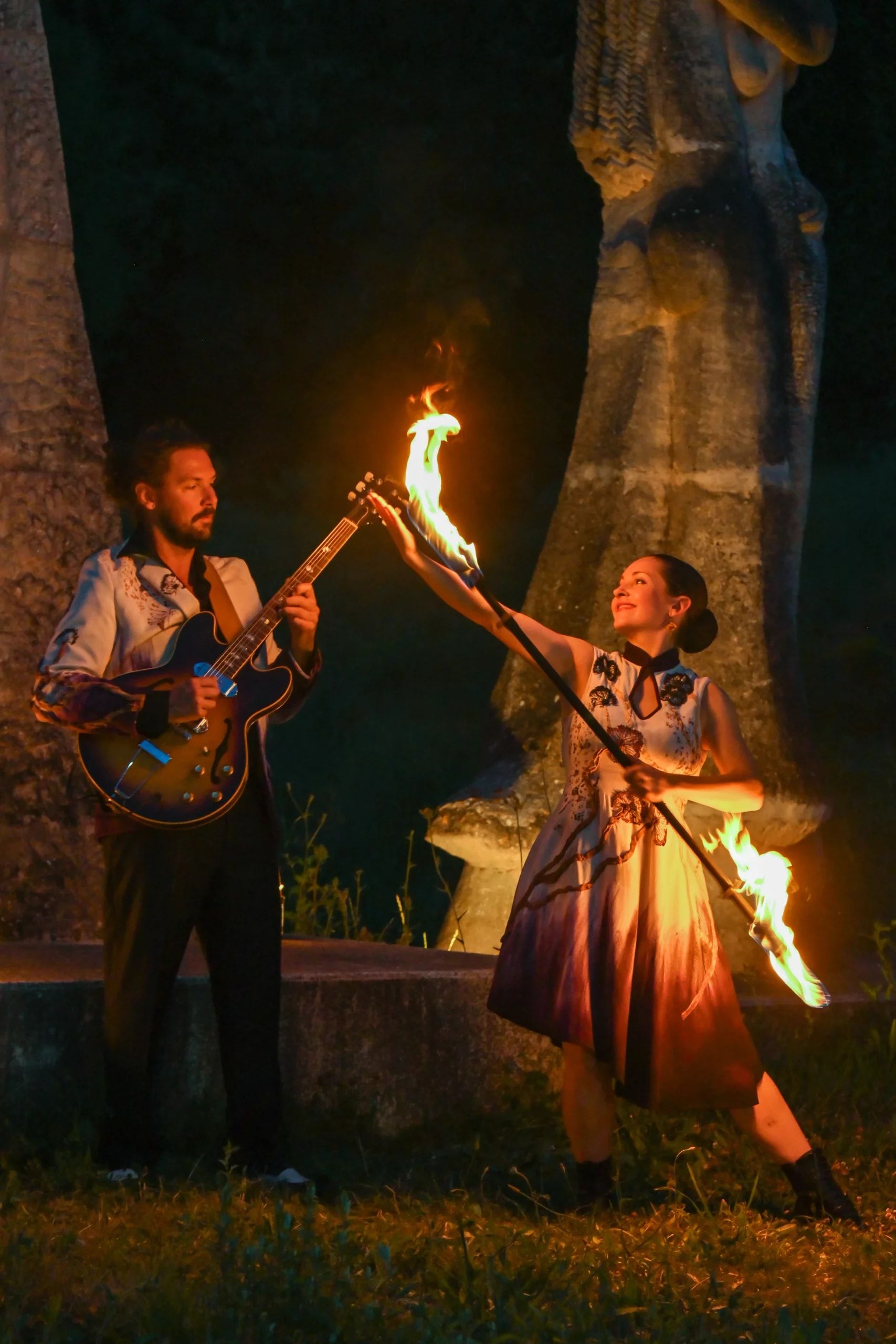 La nuit, la danseuse lève son bâton enflammé vers le guitariste, qui joue à côté d’elle.