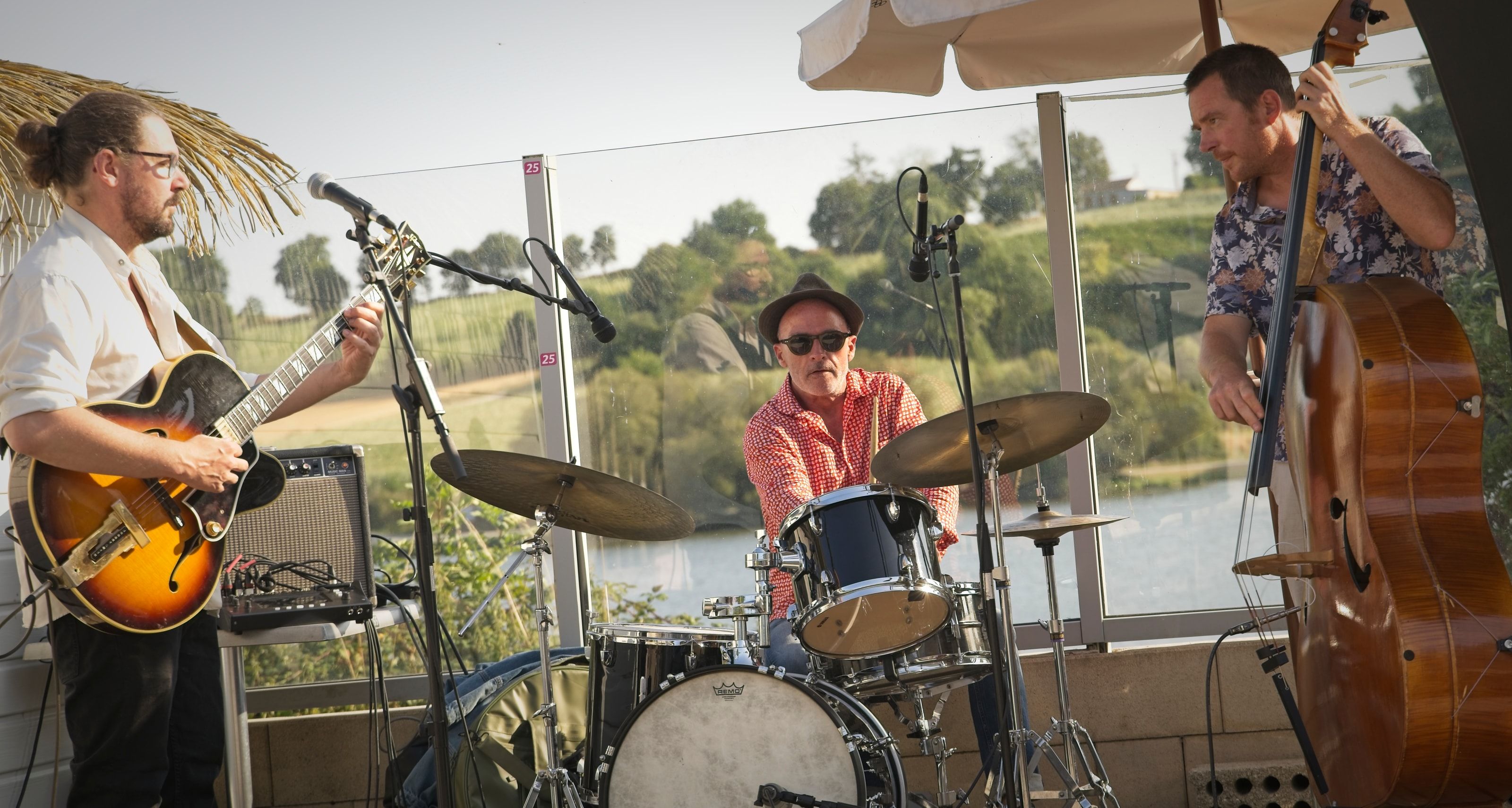 Le Soulful People Trio joue en terrasse au bord de l’eau, en fin de journée, guitare, batterie et contrebasse.